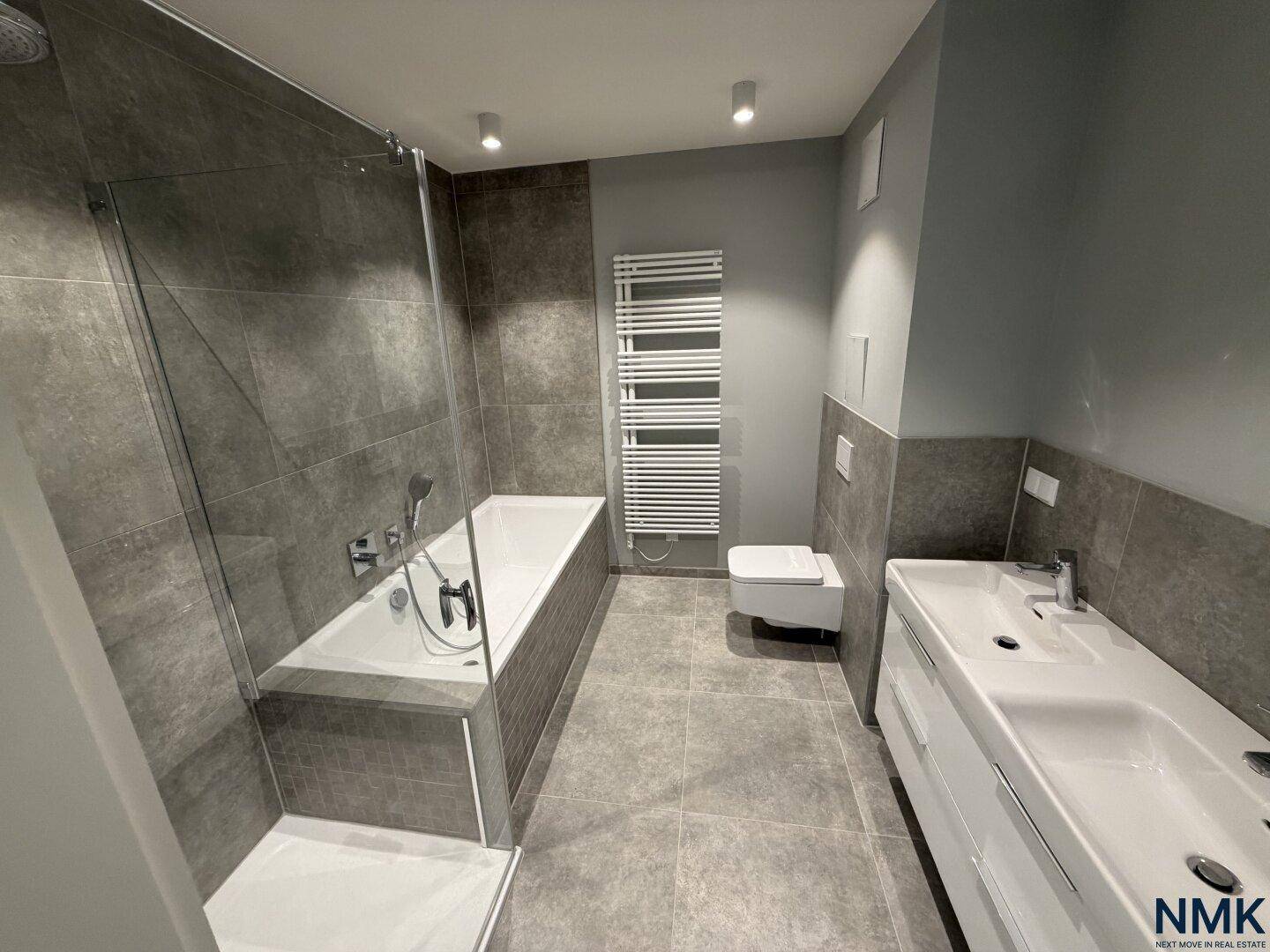 Geräumiges Badezimmer mit Badewanne, Dusche, Doppelwaschbecken und modernen Fliesen.