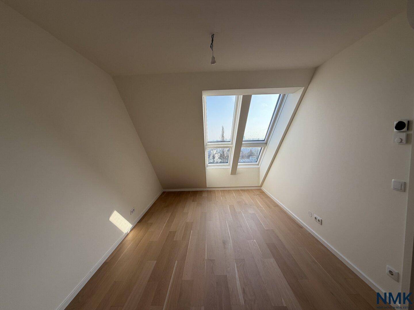 Helles Schlafzimmer im Dachgeschoss mit Holzboden und großen Dachfenstern.