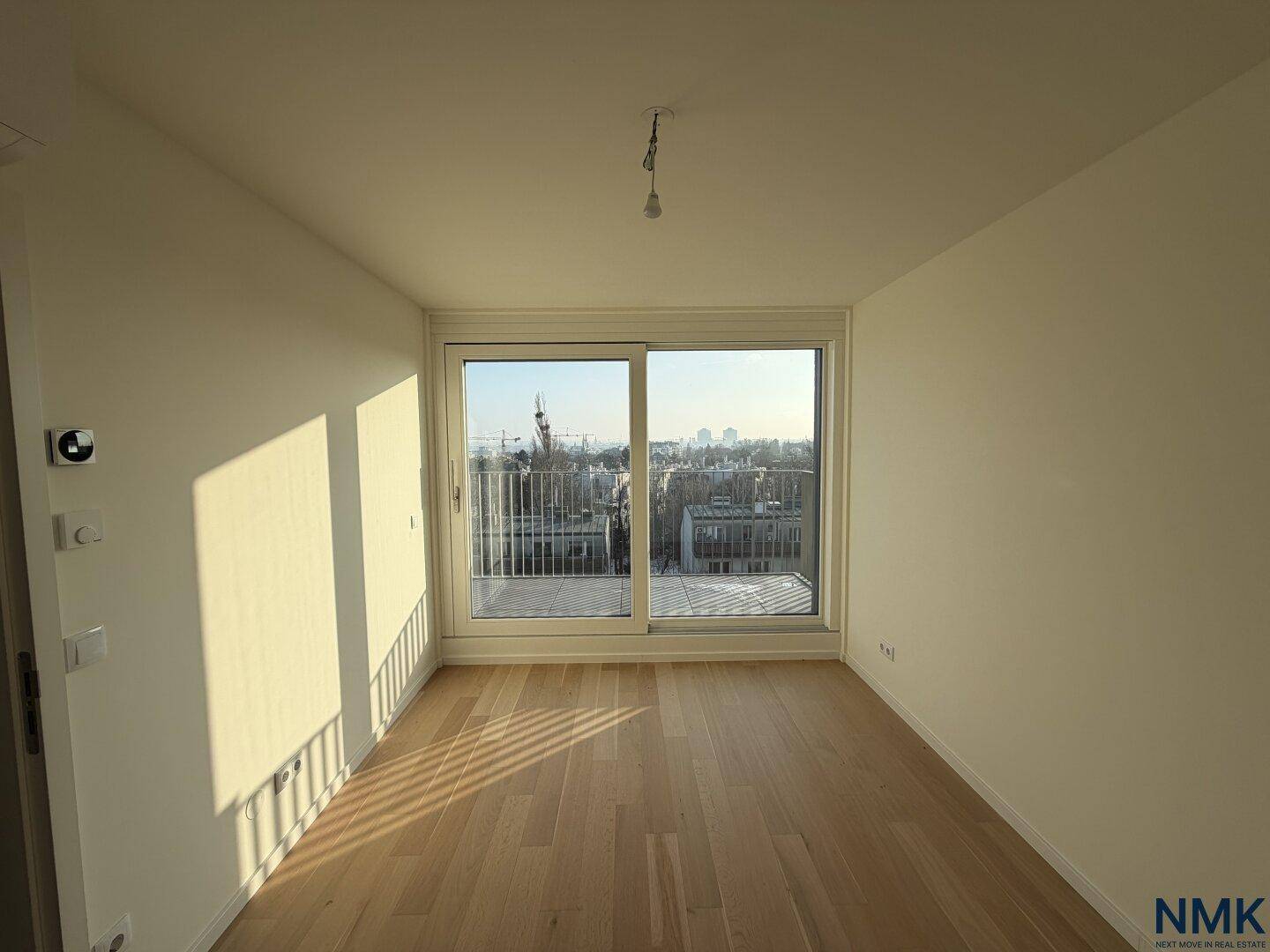 Helles Schlafzimmer mit Holzboden und großem Fenster mit Zugang zu einem Balkon.