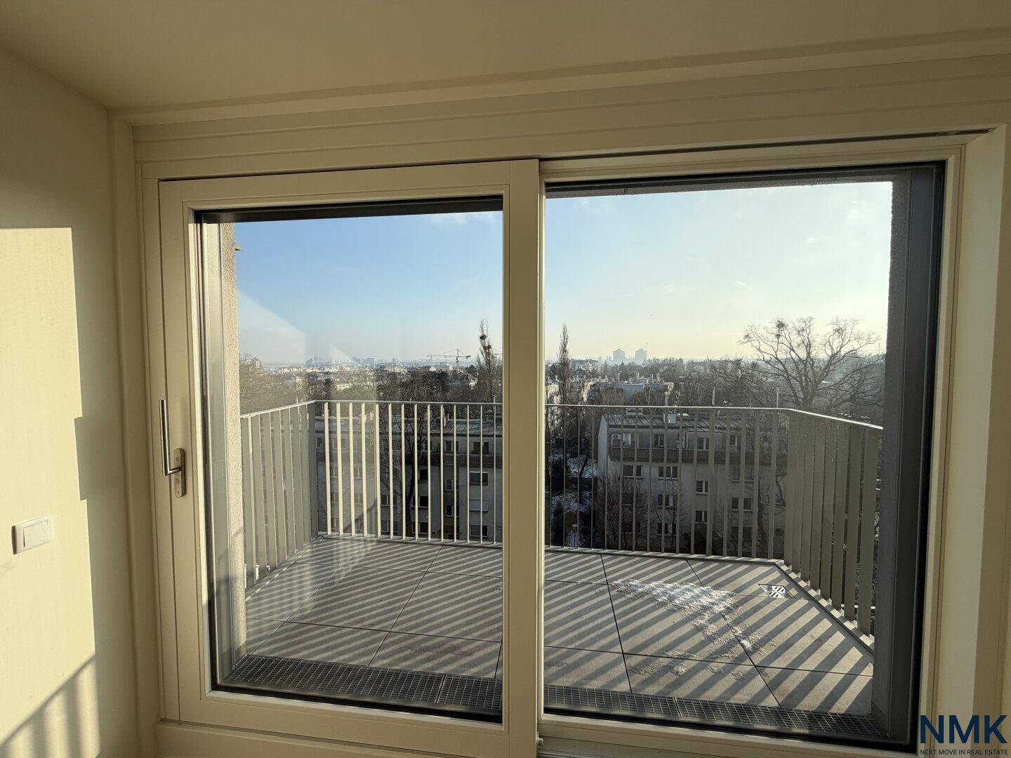 Blick aus dem Fenster auf einen Balkon mit Stadtblick und verschneiter Umgebung.
