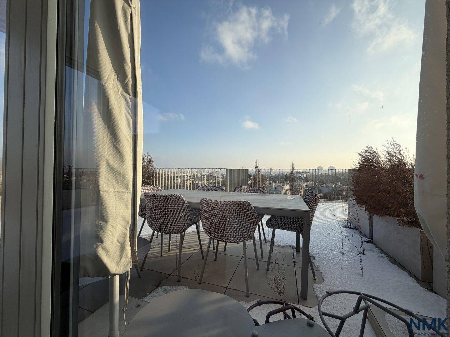 Möblierte Dachterrasse mit Esstisch und Stühlen, umgeben von Schnee und Stadtblick.