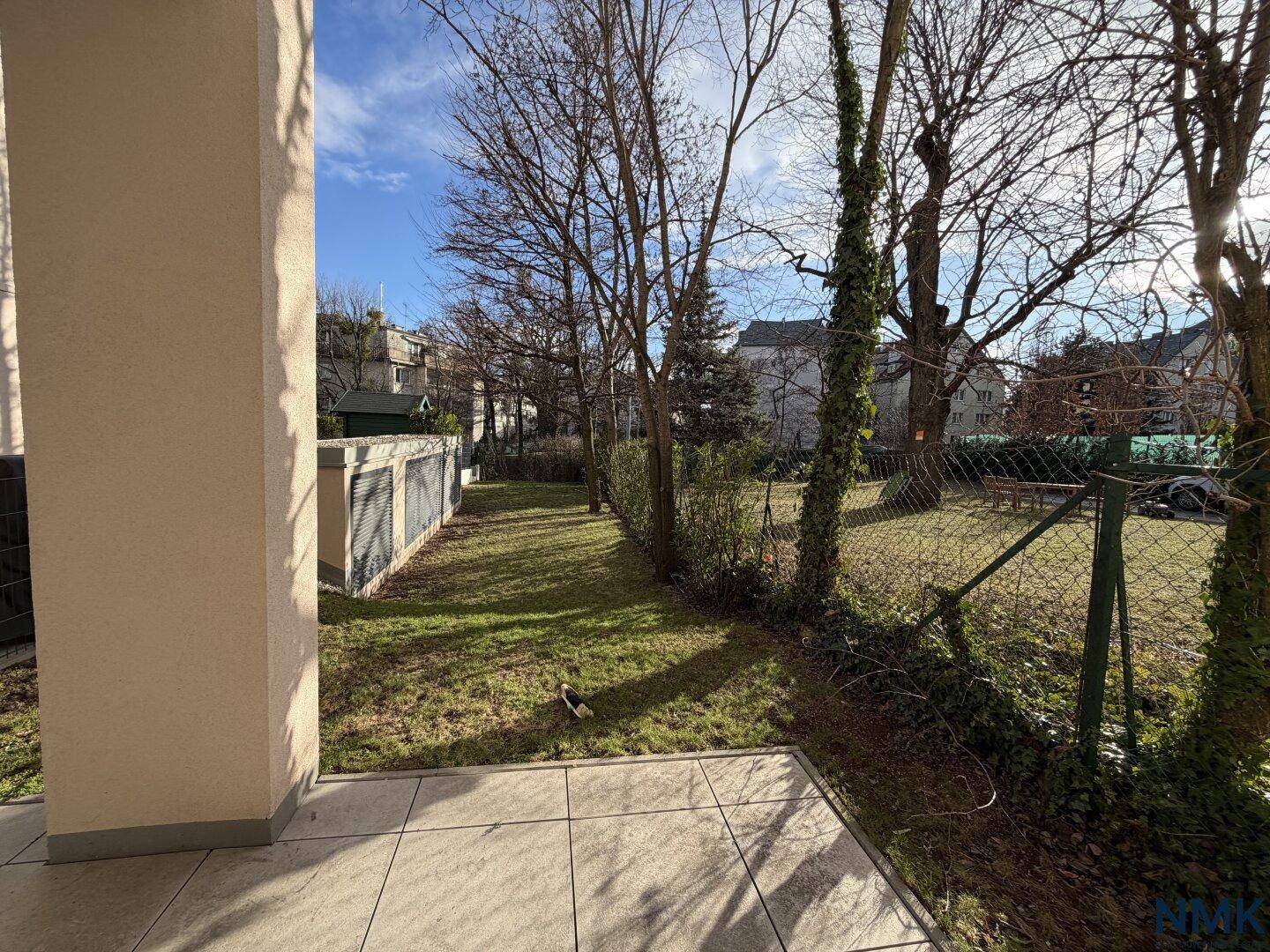 Terrasse mit Fliesenboden und Blick auf den grünen Garten mit Bäumen.