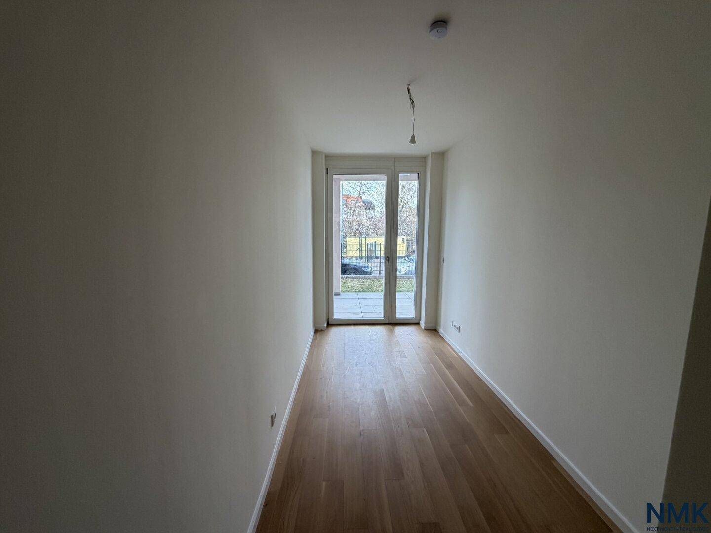 Helles, leeres Zimmer mit Holzboden und Zugang zu einem Außenbereich.