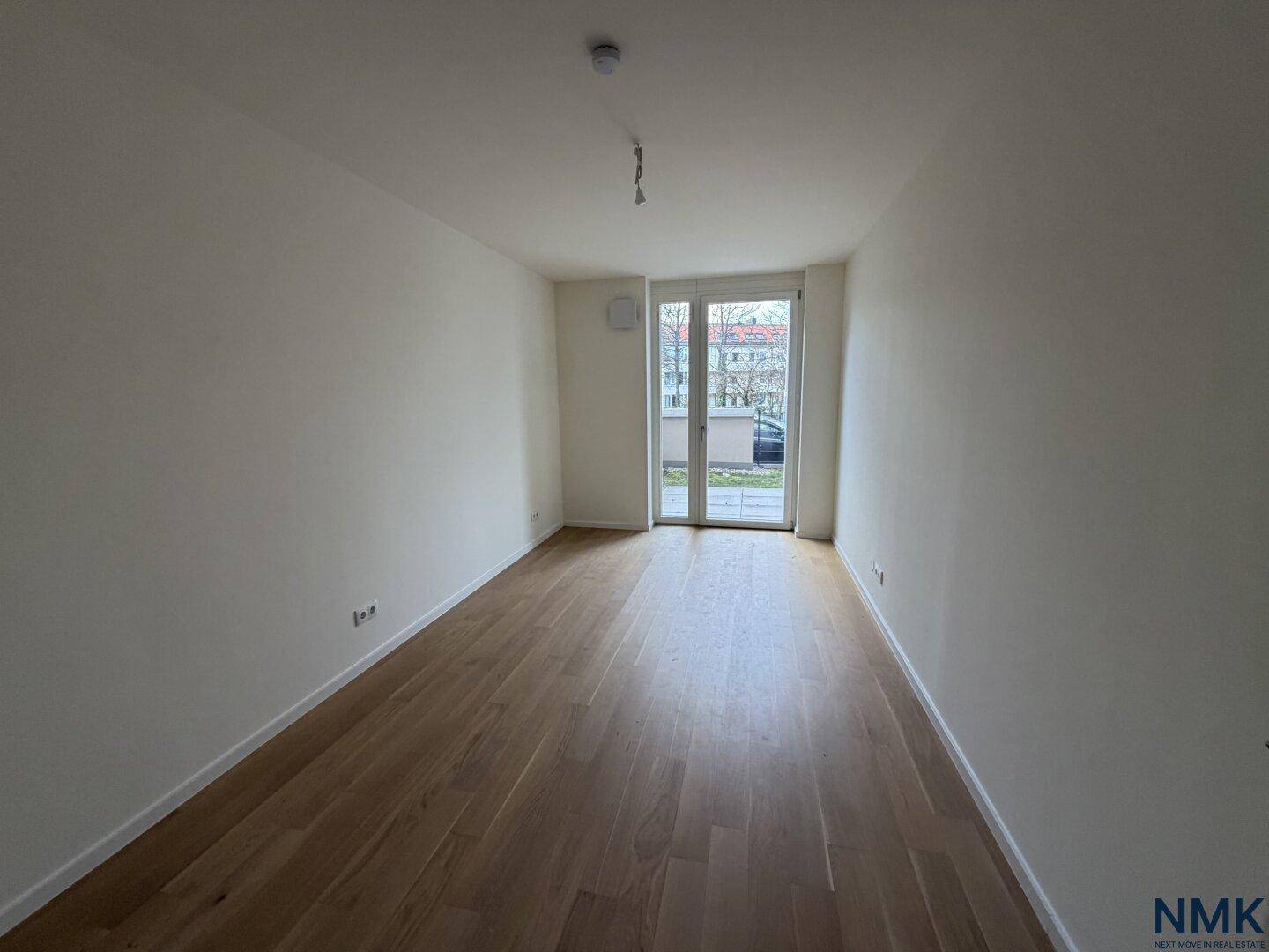 Helles, leeres Zimmer mit Holzboden und Zugang zu einem Außenbereich.