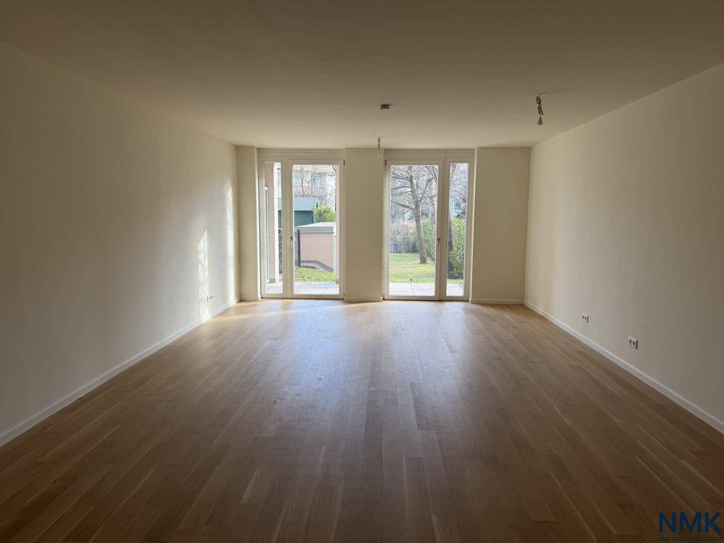 Geräumiges, leeres Wohnzimmer mit hellem Holzboden und direktem Gartenzugang.