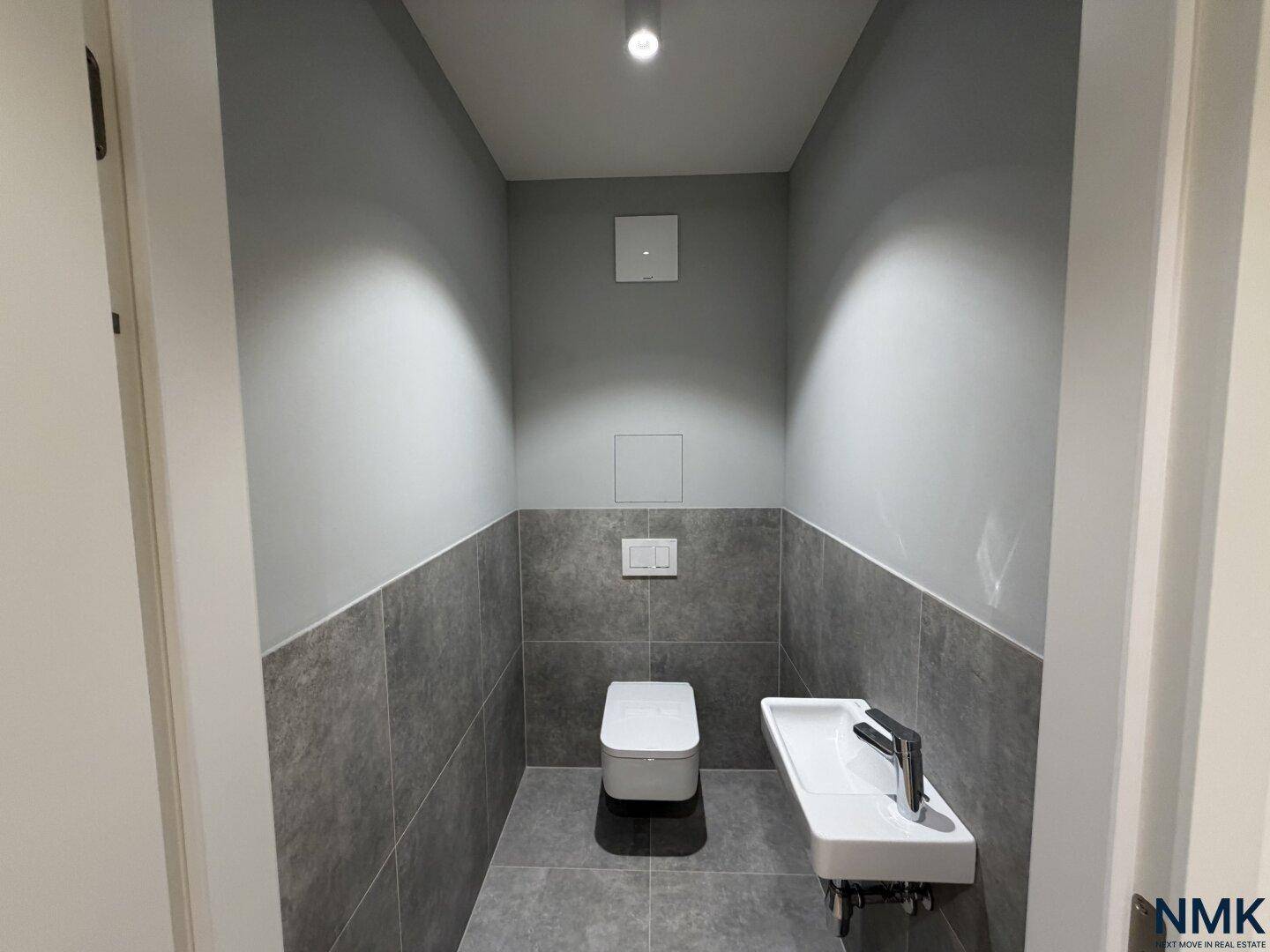 Modernes Gäste-WC mit grauen Fliesen, wandhängendem WC und kleinem Waschbecken.