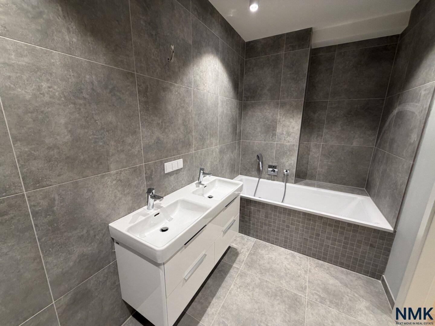 Geräumiges Badezimmer mit Doppelwaschbecken, Badewanne und modernen grauen Fliesen.