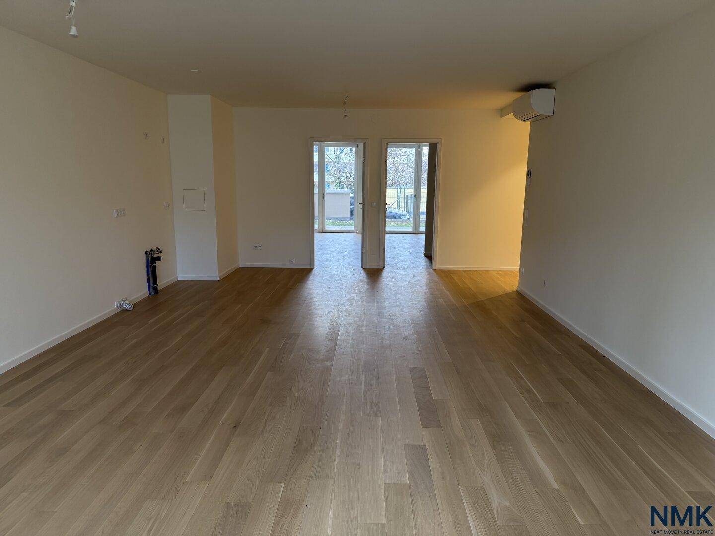 Leerer Raum mit Holzboden und Klimaanlage, der zu weiteren Zimmern führt.