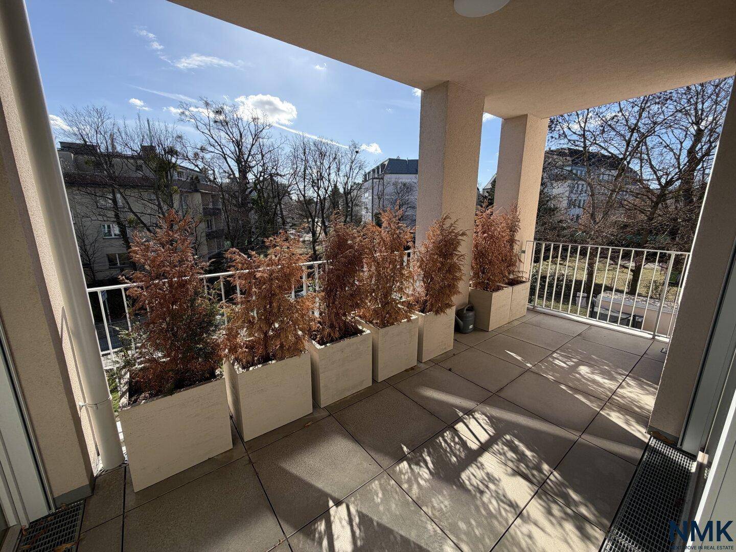 Sonniger Balkon mit Fliesenboden und Pflanzenkübeln, bietet einen Blick ins Grüne.