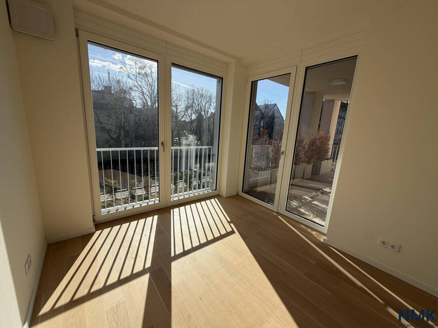 Heller Raum mit Holzboden und großen Fenstern, die viel Tageslicht hereinlassen.