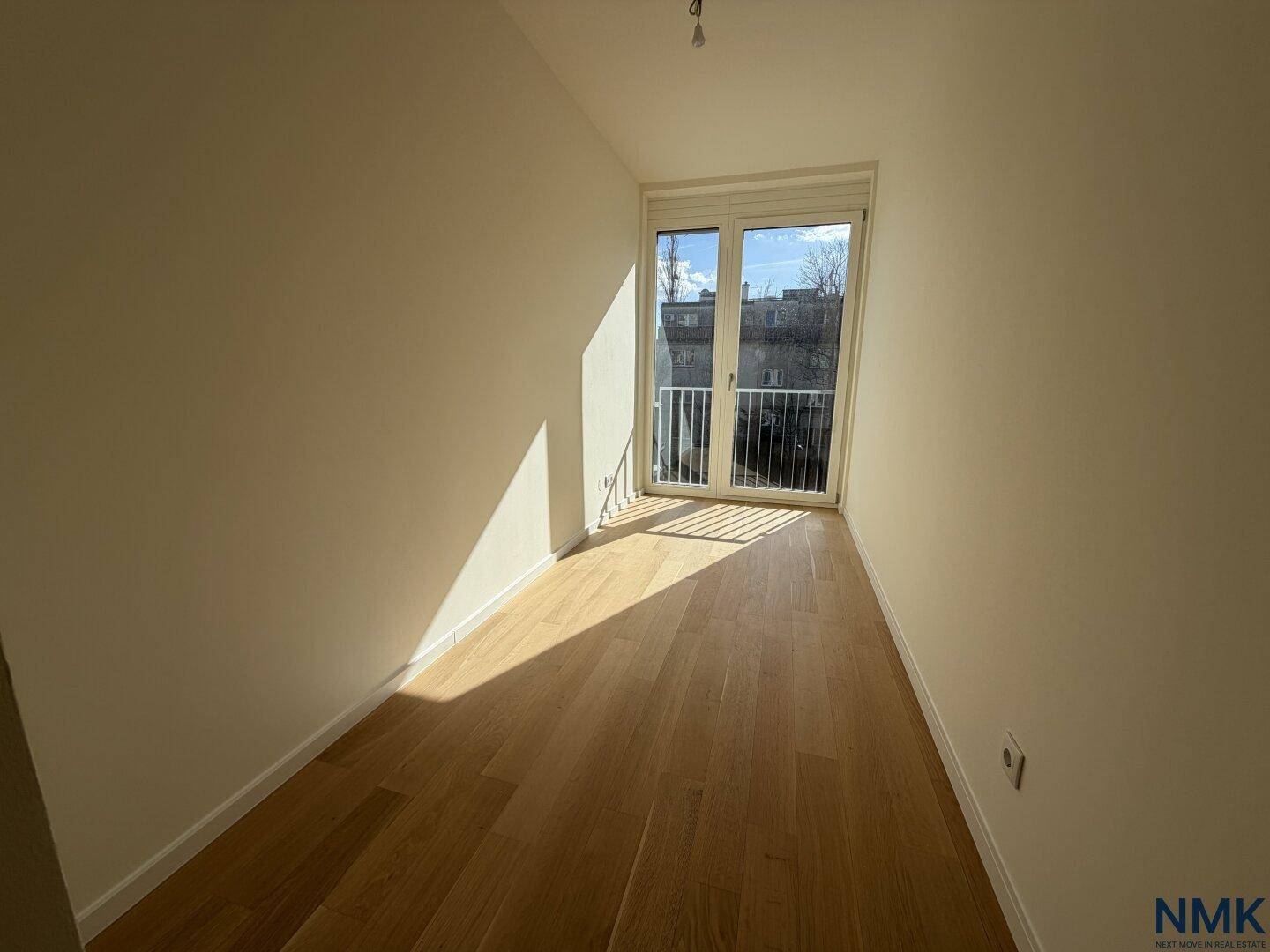 Schmaler, heller Raum mit Holzboden und französischem Balkon, vielseitig nutzbar.
