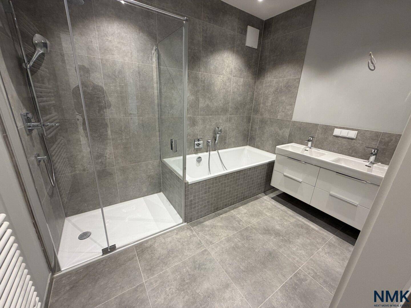 Modernes Badezimmer mit grauen Fliesen, Dusche, Badewanne und Doppelwaschbecken.