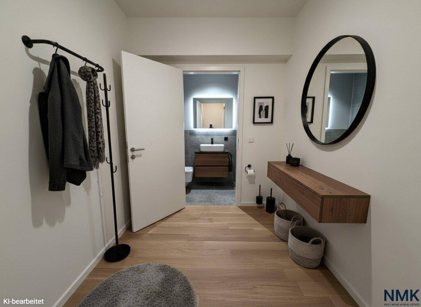 Moderner Flur mit Garderobe, Spiegel und Holzboden, der zum Badezimmer führt.