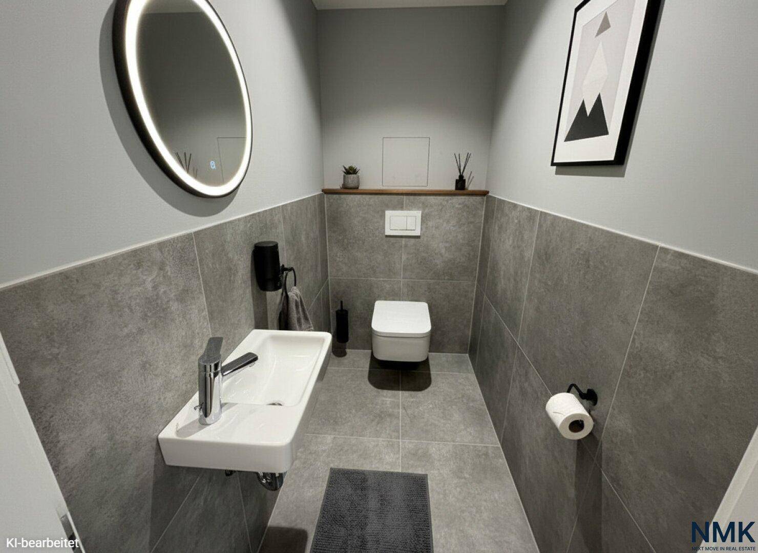 Stilvolles Gäste-WC mit grauen Fliesen, rundem Spiegel und moderner Dekoration.