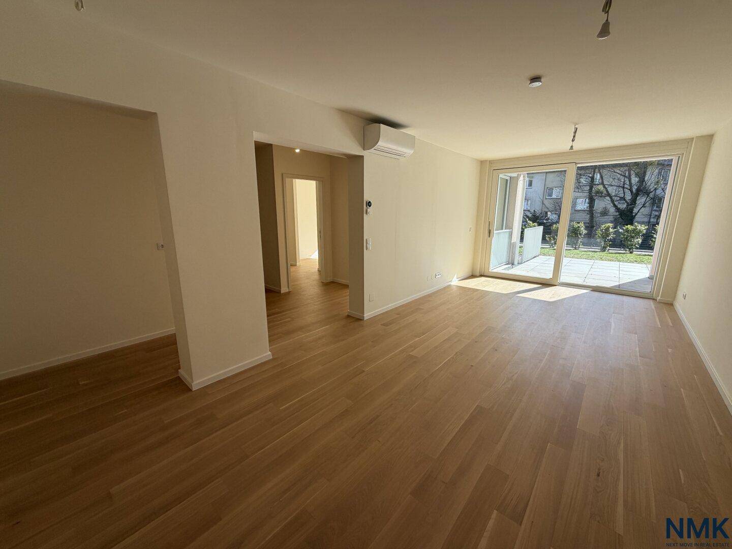 Geräumiger, leerer Wohn- und Essbereich mit Holzboden und großen Fenstern zur Terrasse.