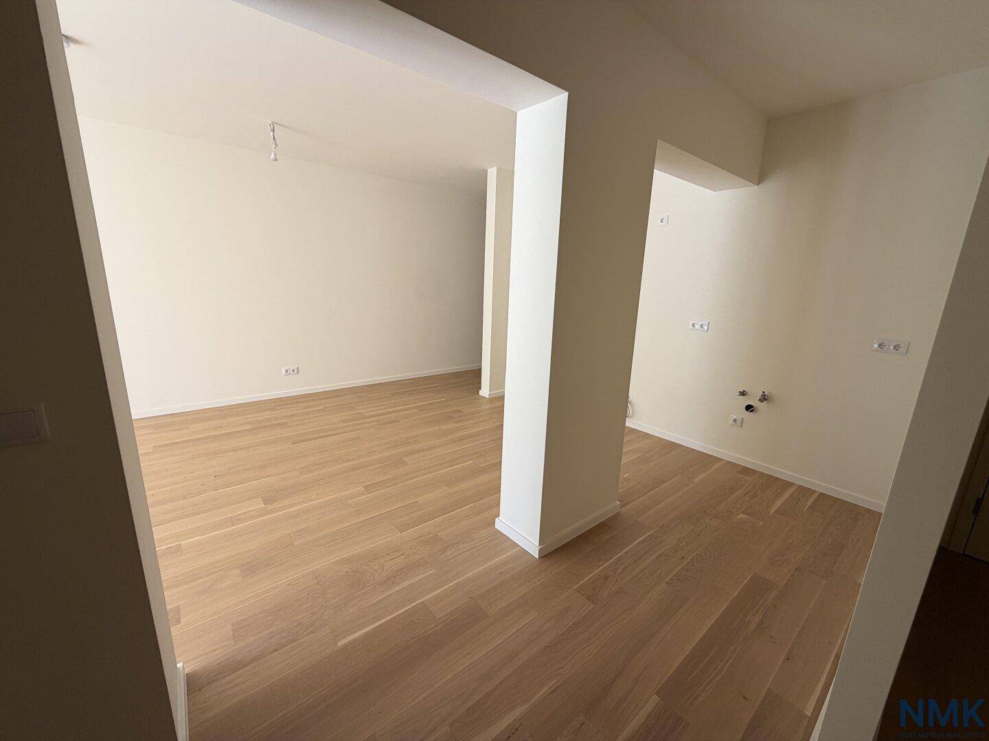 Leerer Küchenbereich mit Holzboden und Anschlüssen, bereit für die Installation einer Einbauküche.