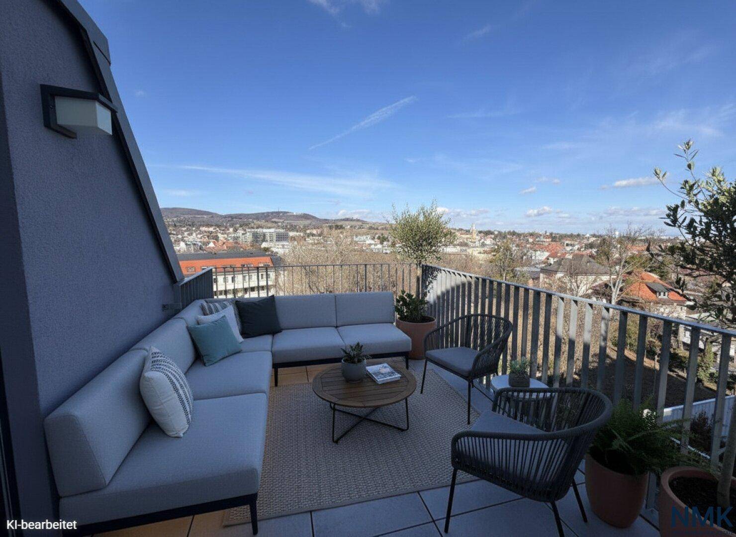 Möblierter Balkon mit gemütlicher Sitzecke, Pflanzen und Panoramablick auf die Stadt und die Berge.