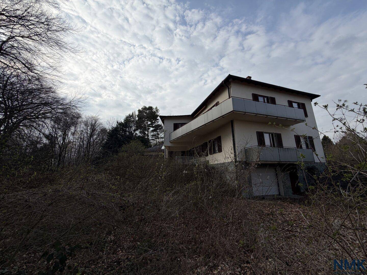 Seitenansicht des Hauses mit mehreren Balkonen und umgebender, wilder Vegetation.