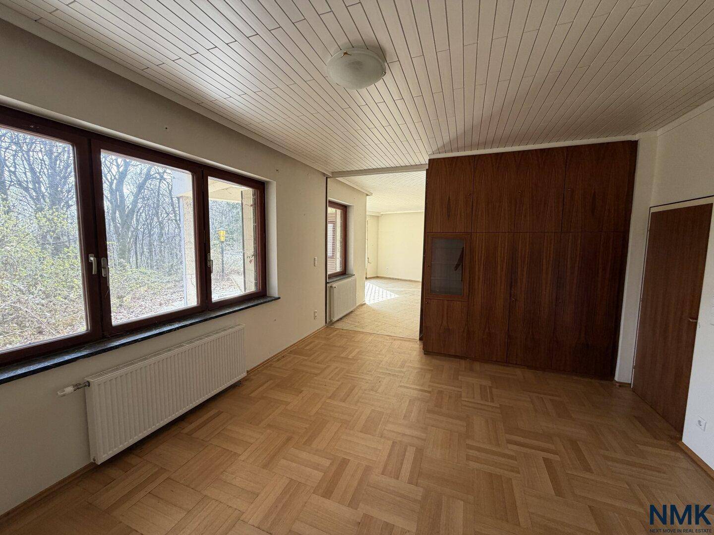 Leerer Raum mit Parkettboden und einer Holzwandverkleidung, angrenzend an einen weiteren Raum.
