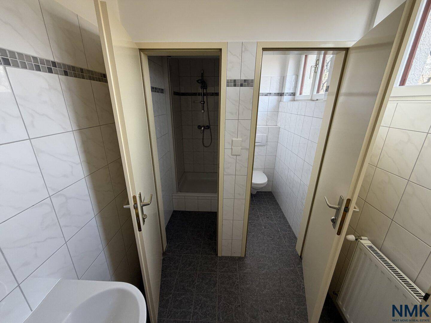 Badezimmer mit separaten Dusch- und WC-Bereichen, komplett gefliest in hellen Tönen.