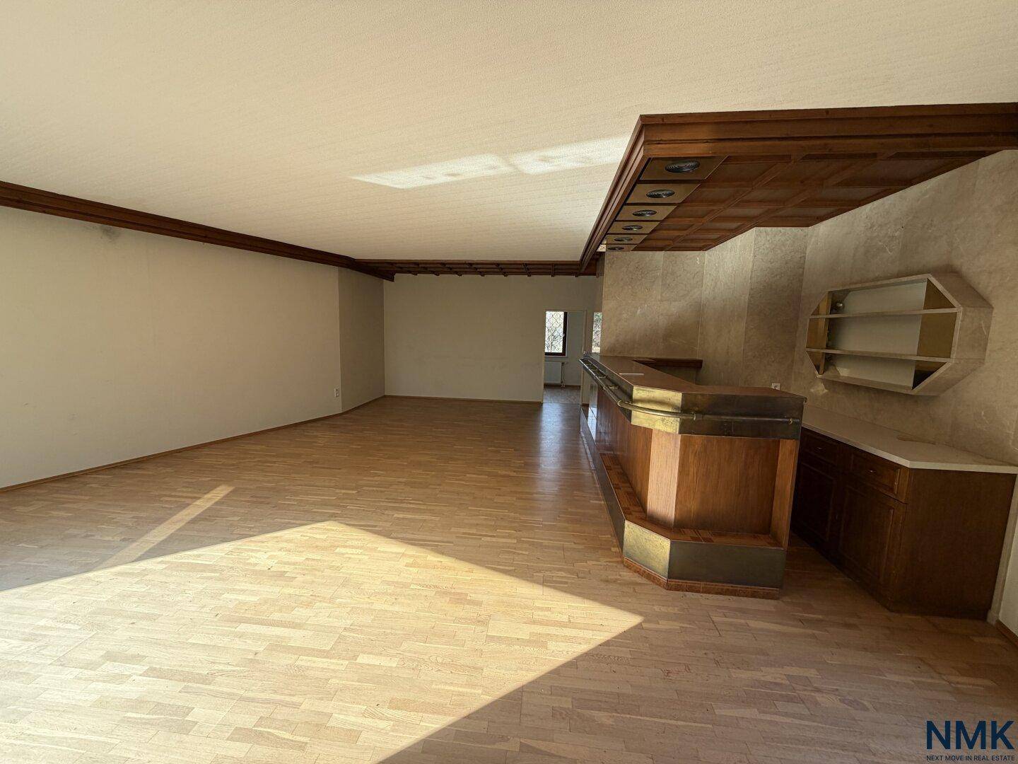 Geräumiger leerer Raum mit Holzfußboden, einer eingebauten Bar und Holzelementen an der Decke.