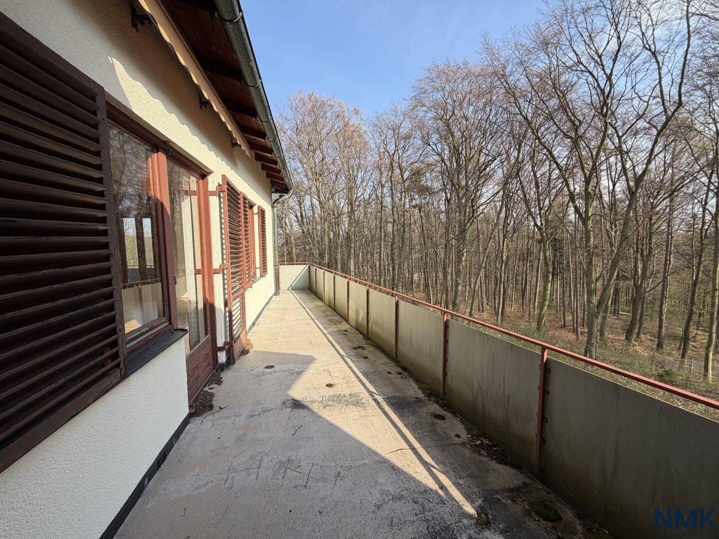 Langer, schmaler Balkon mit Betonboden und Blick auf den umliegenden Wald.