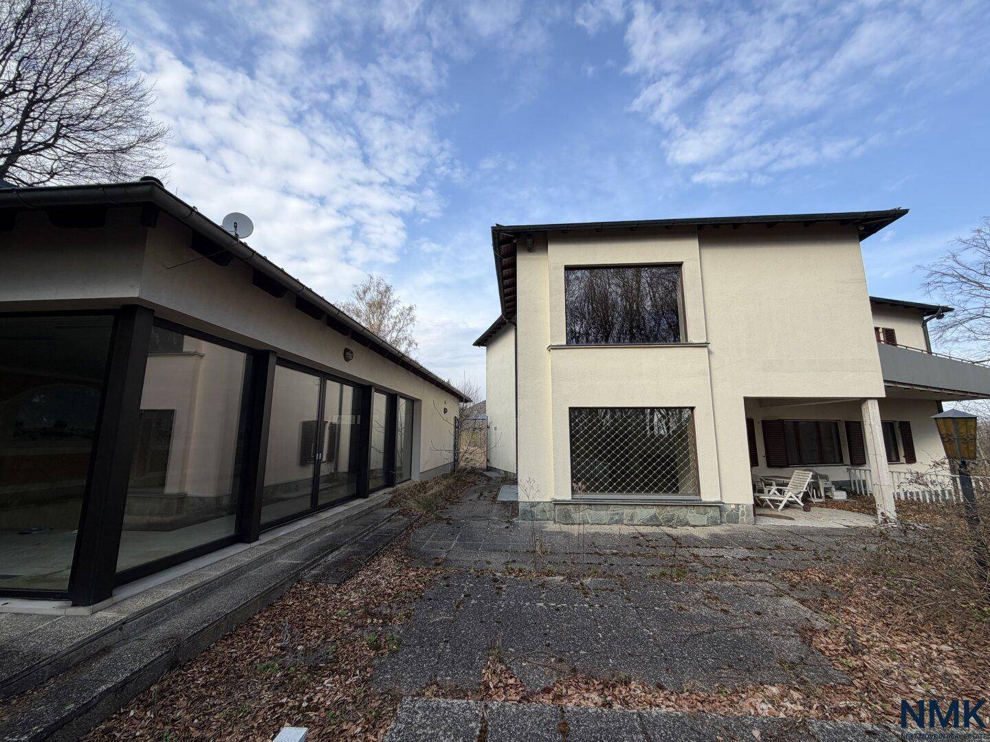Ansicht des Haupthauses und eines Nebengebäudes mit großen Glasfronten und Terrasse.
