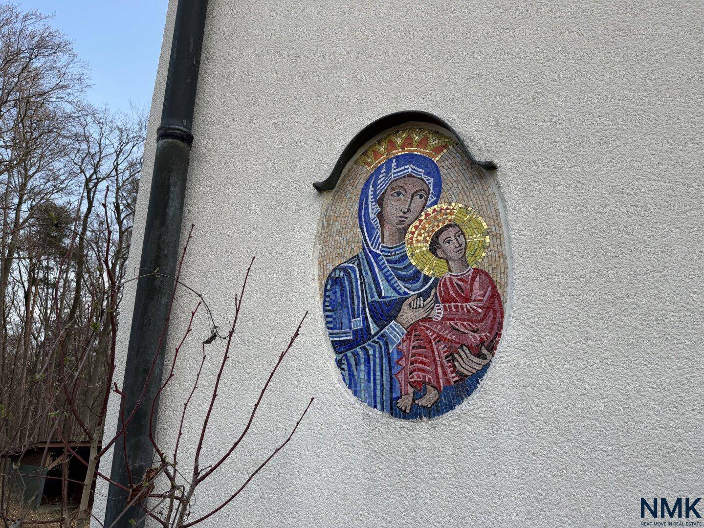 Außenwand des Gebäudes mit einem Mosaikbild der Madonna mit Kind, umgeben von Bäumen.