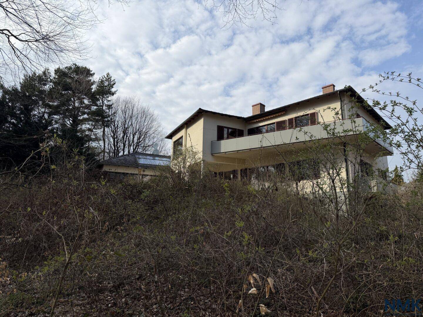 Außenansicht des Hauses, teilweise von Büschen verdeckt, mit Blick auf die umgebende Natur.