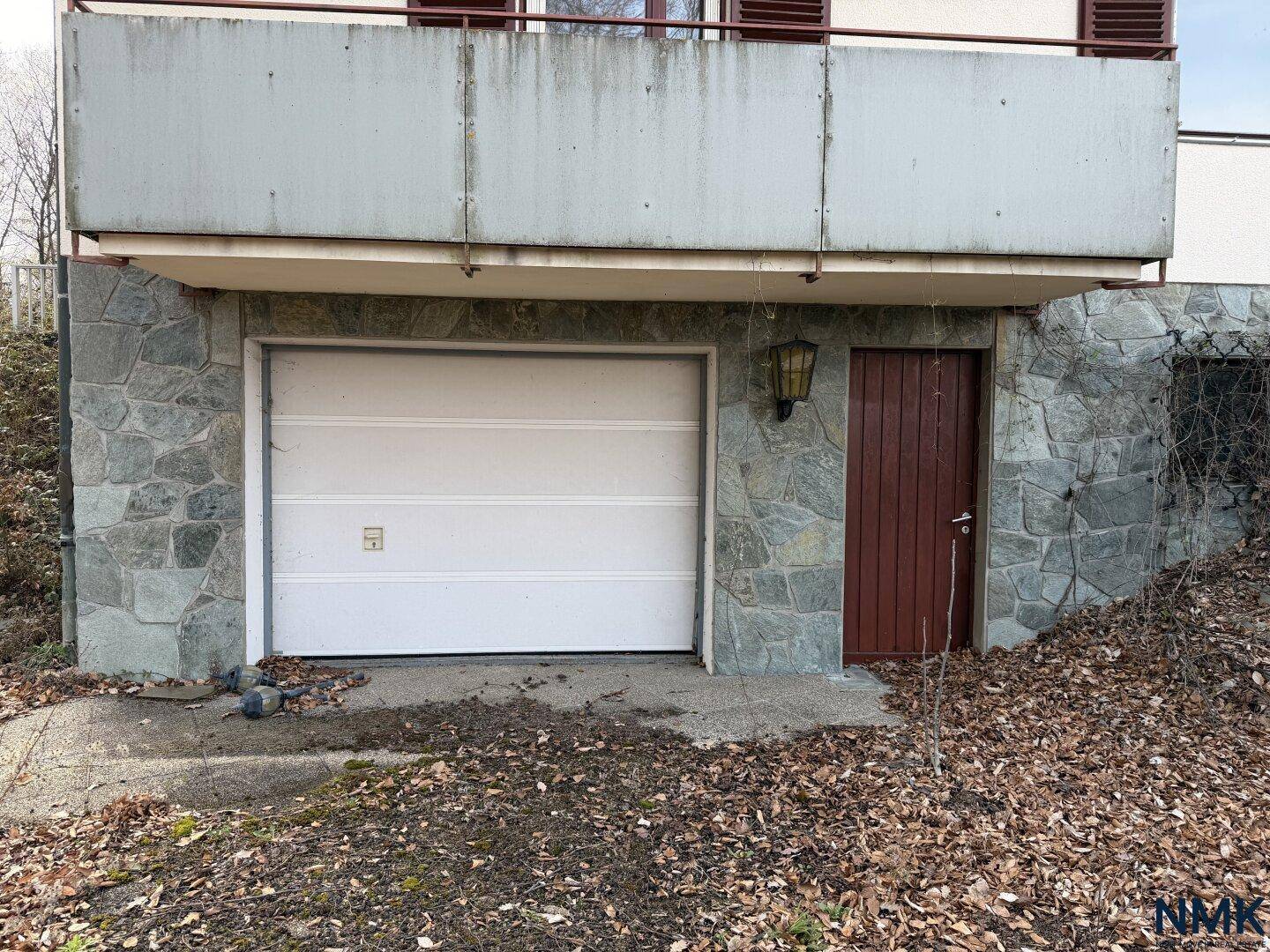 Garagentor und Holztür in einer steinverkleideten Wand unter einem Balkon.