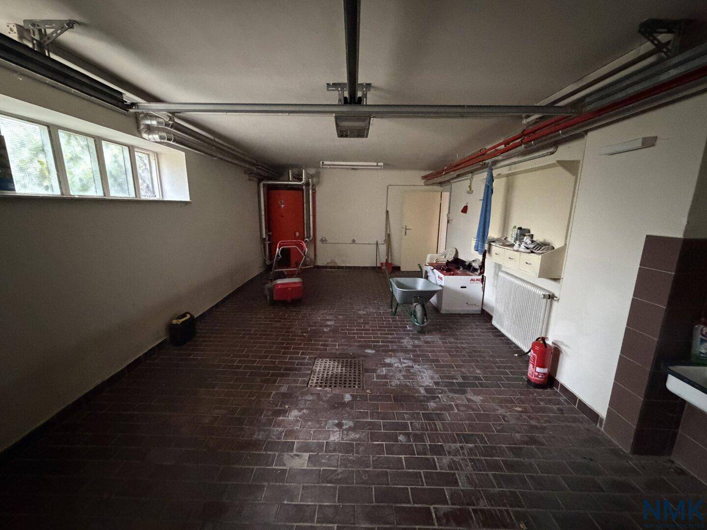 Innenansicht der Garage mit Betonboden, sichtbaren Rohren und verschiedenen Werkzeugen.
