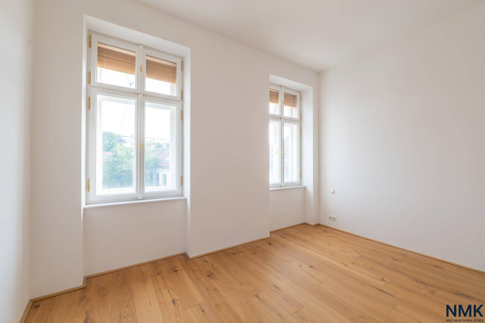 Helles Zimmer mit zwei Fenstern und Holzboden, ideal als Schlaf- oder Arbeitszimmer.