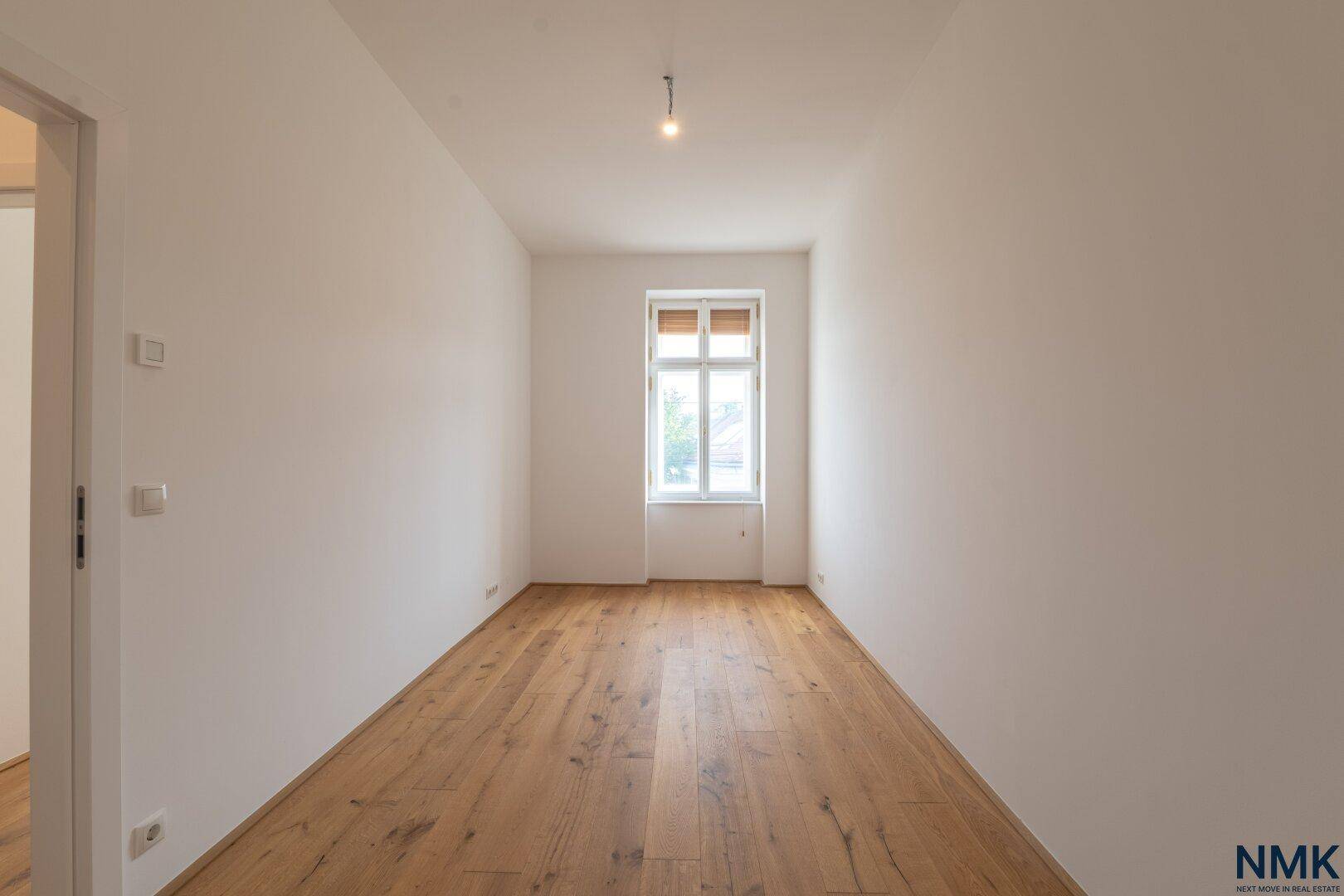 Langes, helles Zimmer mit Holzboden und einem Fenster, vielseitig nutzbar.