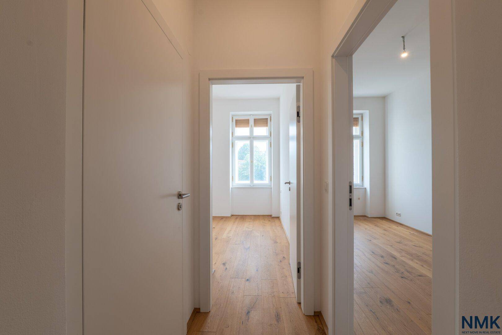 Heller Flur mit Holzboden, der zu weiteren Zimmern mit Fenstern führt.