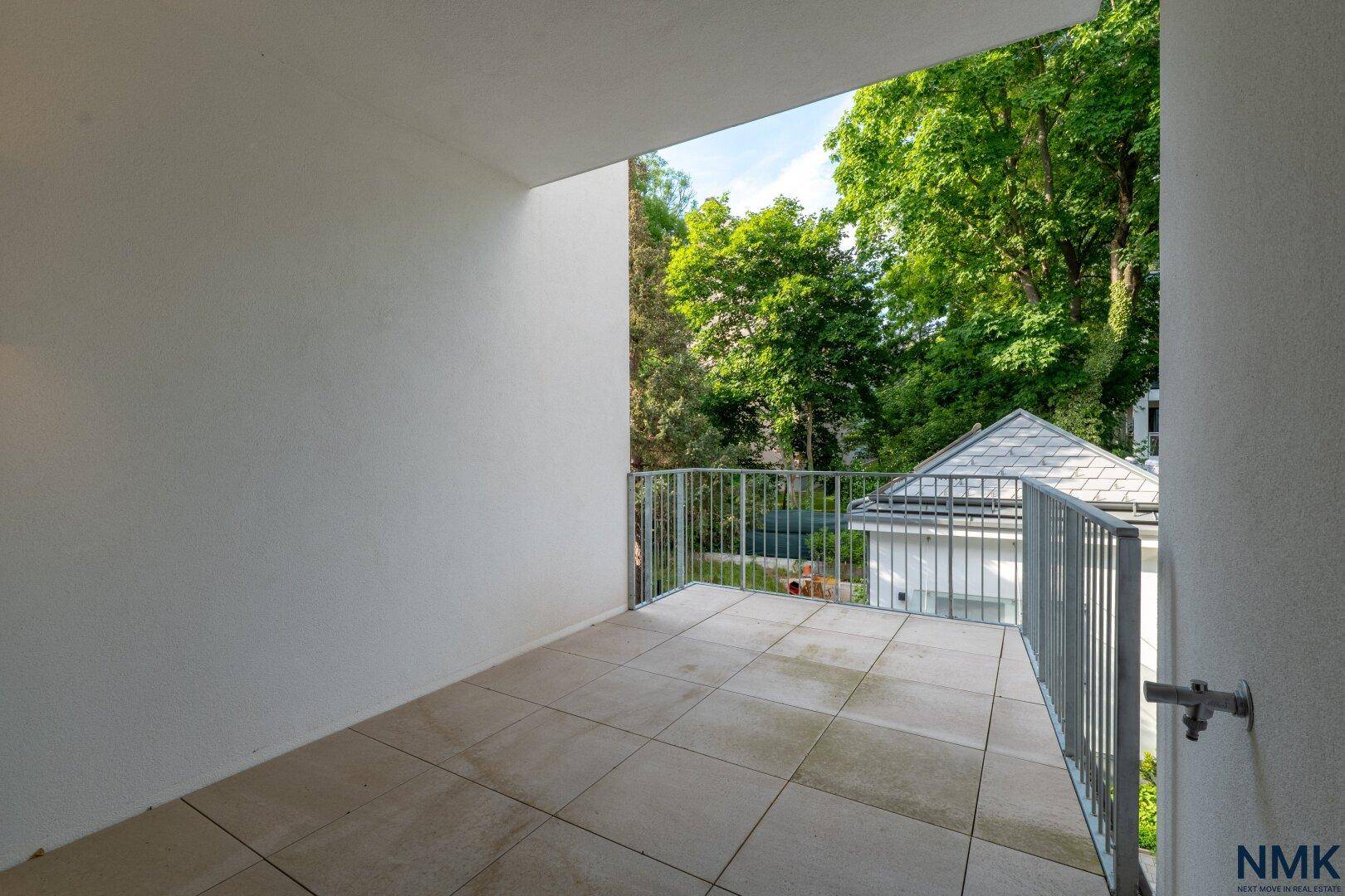Geräumiger Balkon mit Fliesenboden und Blick ins Grüne, umgeben von Bäumen.