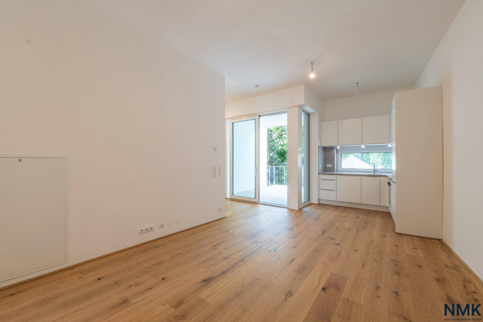 Heller Wohnbereich mit Holzboden und offener Küche, die zum Außenbereich führt.