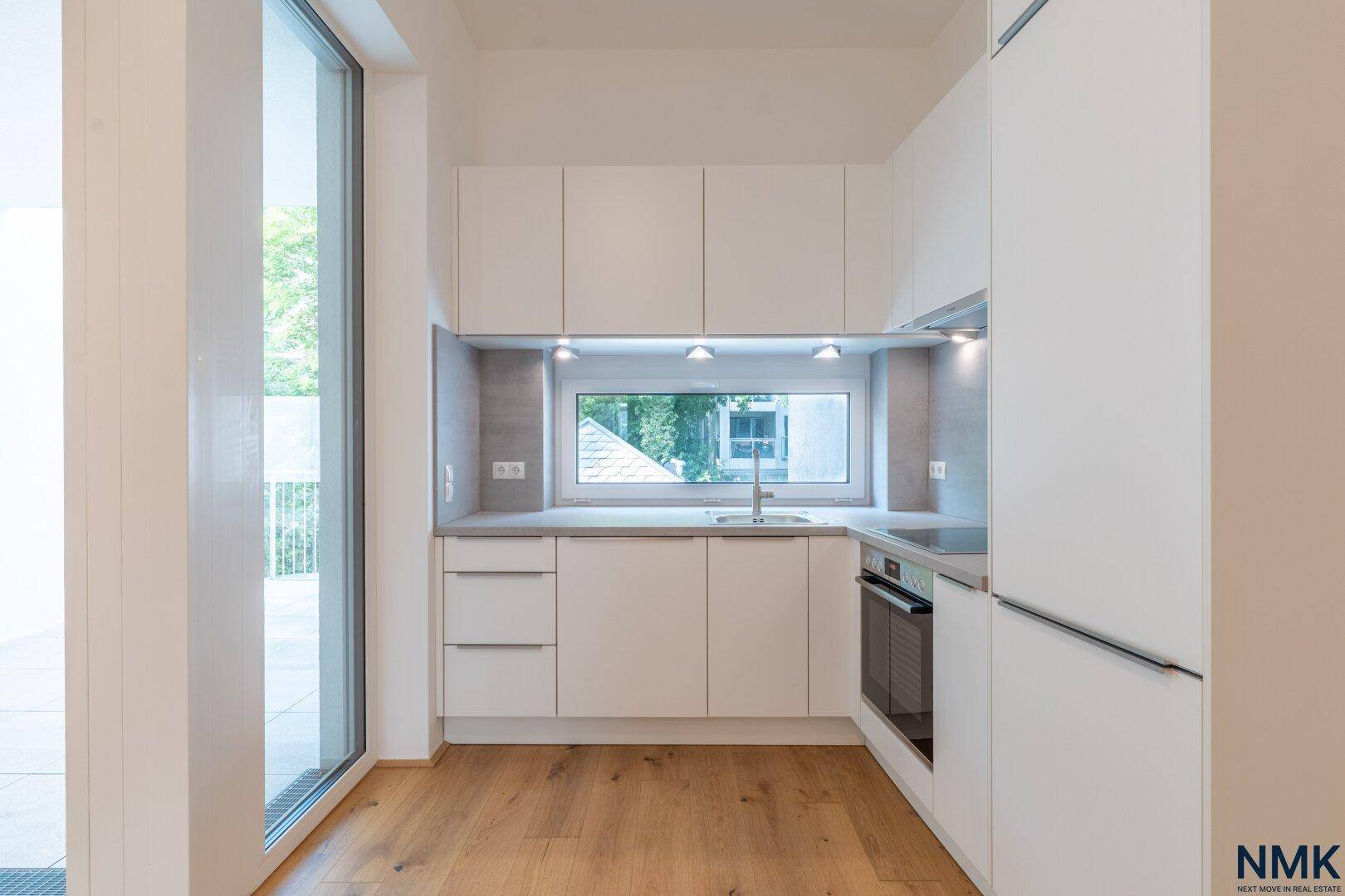 Nahaufnahme der modernen weißen Küche mit integriertem Backofen und Fenster über der Spüle.
