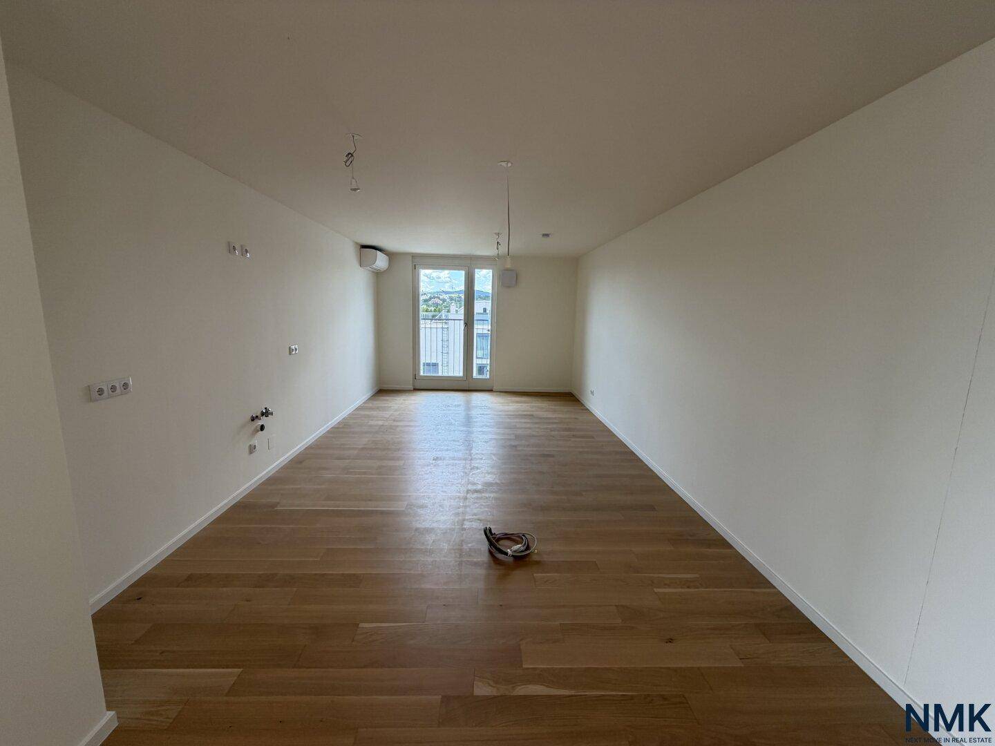 Leerer Raum mit Holzboden, weißen Wänden und Zugang zu einem Balkon.