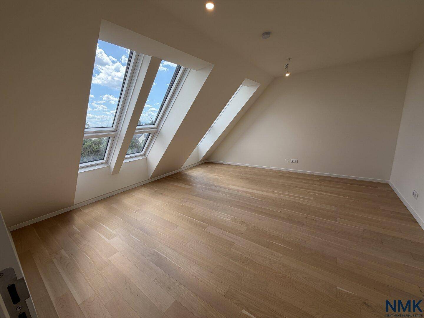 Leeres Schlafzimmer mit Holzboden, Dachschrägen und großen Dachfenstern.