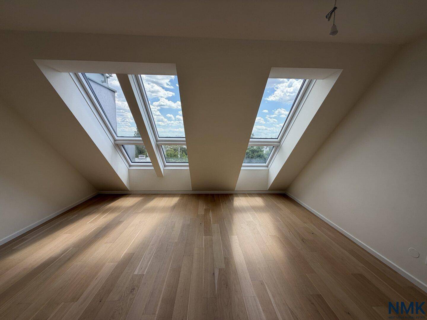 Leeres Schlafzimmer mit Holzboden, Dachschrägen und zwei großen Dachfenstern.