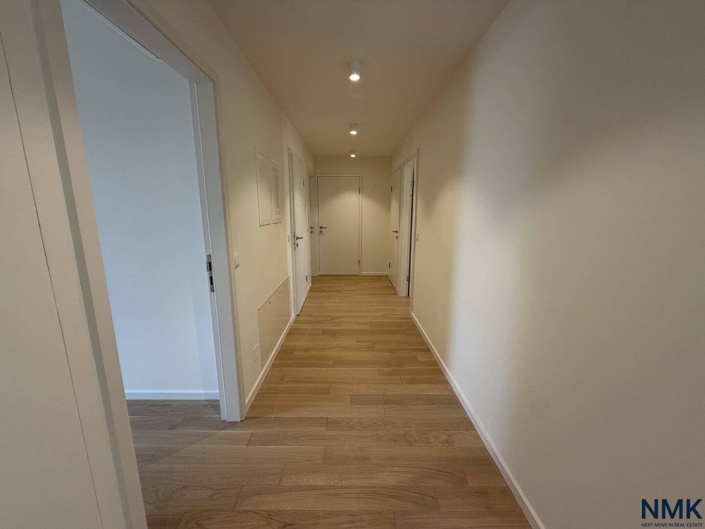 Heller Flur mit Holzboden, weißen Wänden und mehreren Türen.