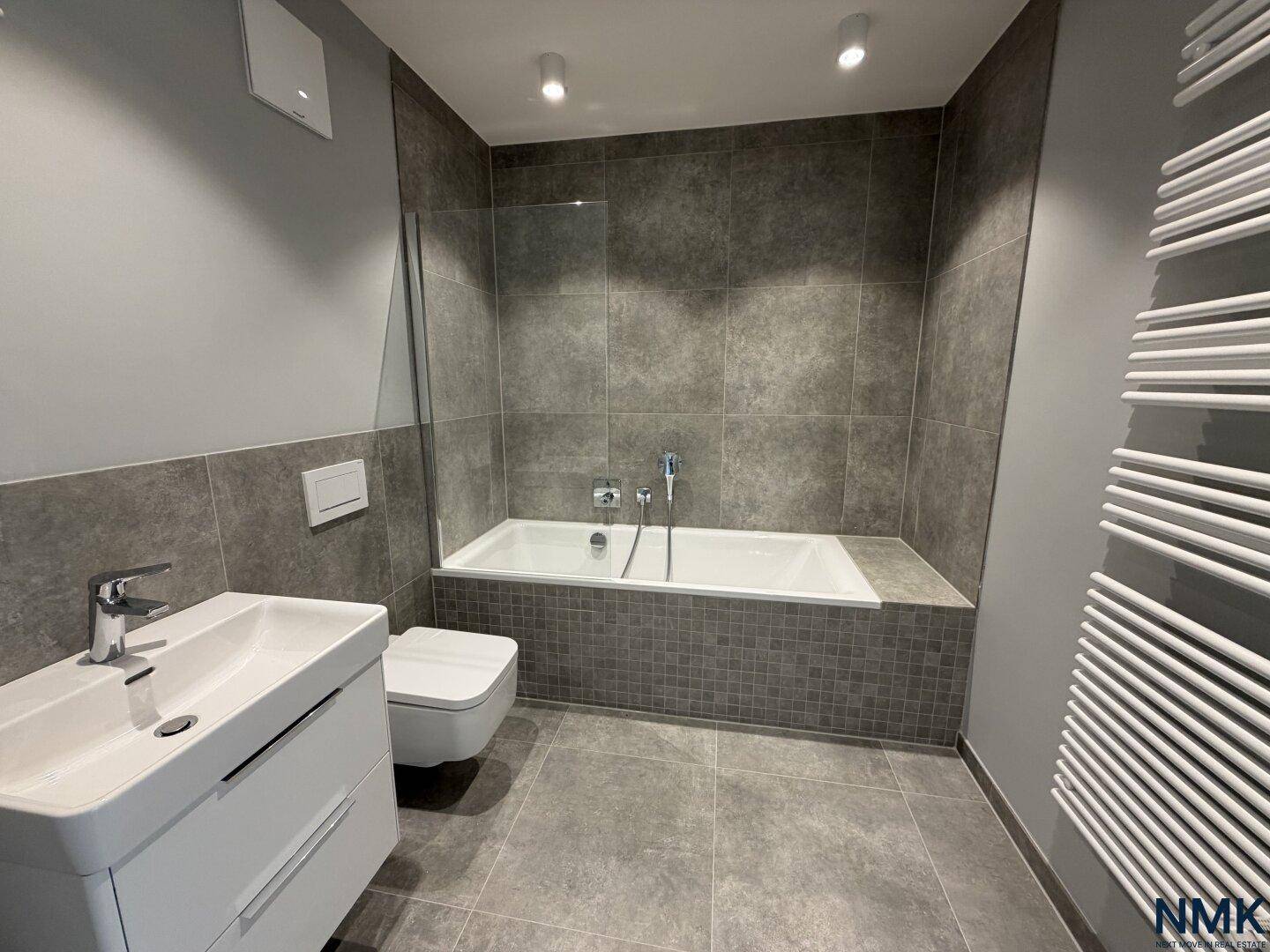 Modernes Badezimmer mit Badewanne, Einzelwaschbecken und grauen Fliesen.