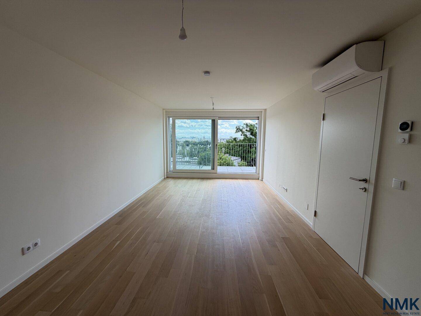 Leeres Wohnzimmer mit Holzboden, weißen Wänden und großem Fenster mit Stadtblick.