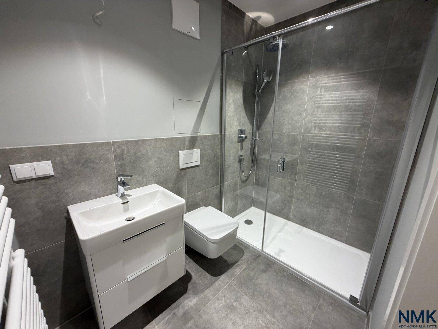 Modernes Badezimmer mit Duschkabine, Einzelwaschbecken und grauen Fliesen.