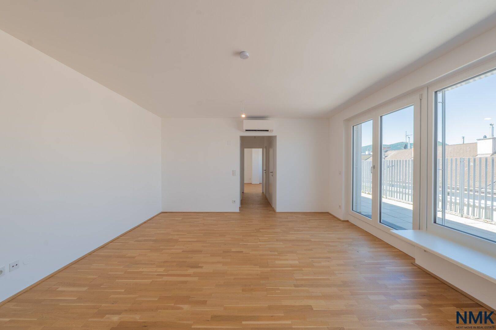 Helles, leeres Wohnzimmer mit Parkettboden, großen Fenstern und Zugang zur Terrasse.