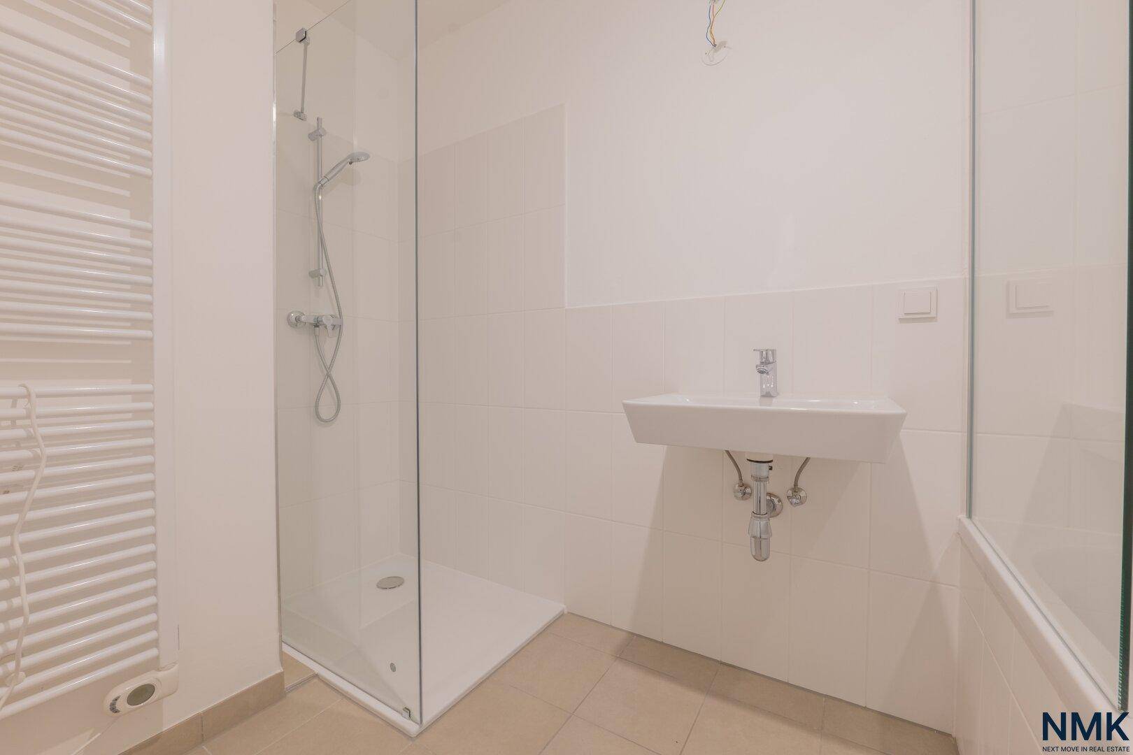 Helles Badezimmer mit ebenerdiger Dusche, Glasabtrennung, Einzelwaschbecken und Handtuchheizkörper.