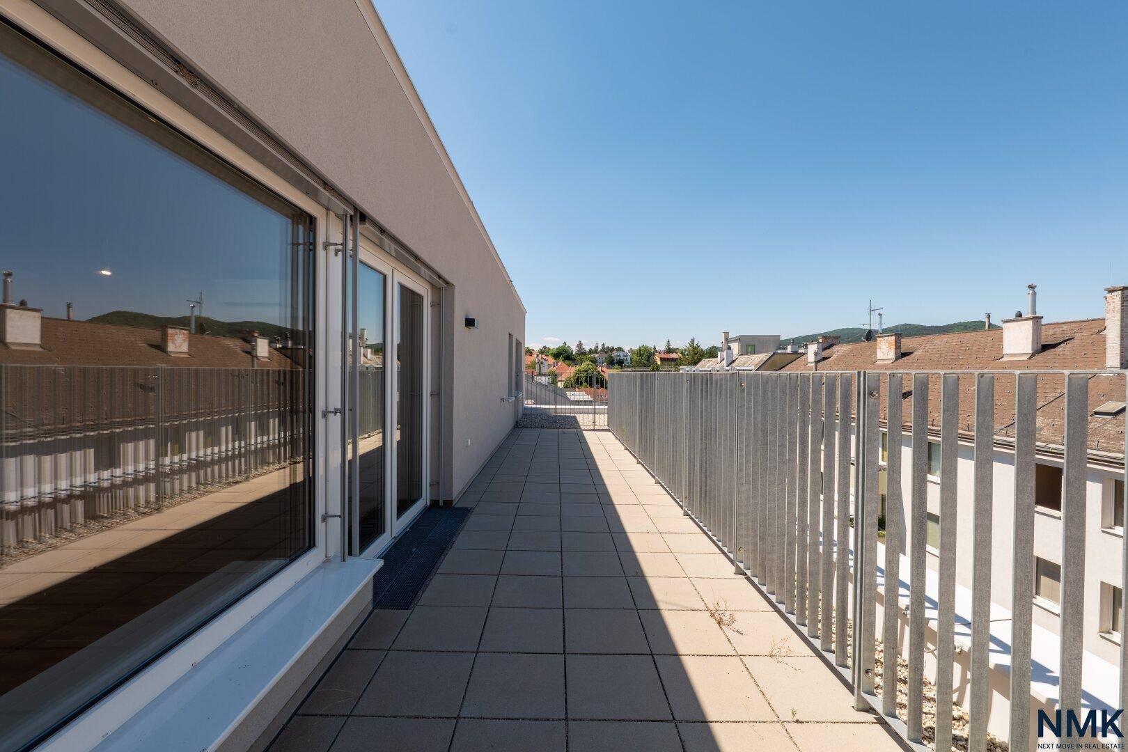 Langer, schmaler Terrassenbereich mit Fliesenboden und Blick auf die umliegenden Dächer.