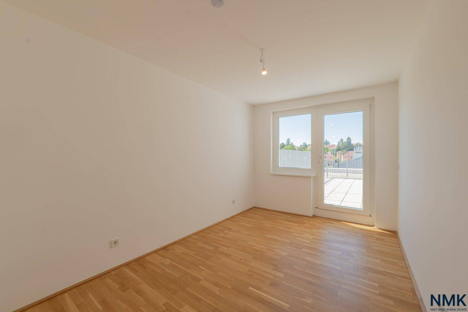 Unmöbliertes Schlafzimmer mit Parkettboden, weißen Wänden und Zugang zu einem Außenbereich.