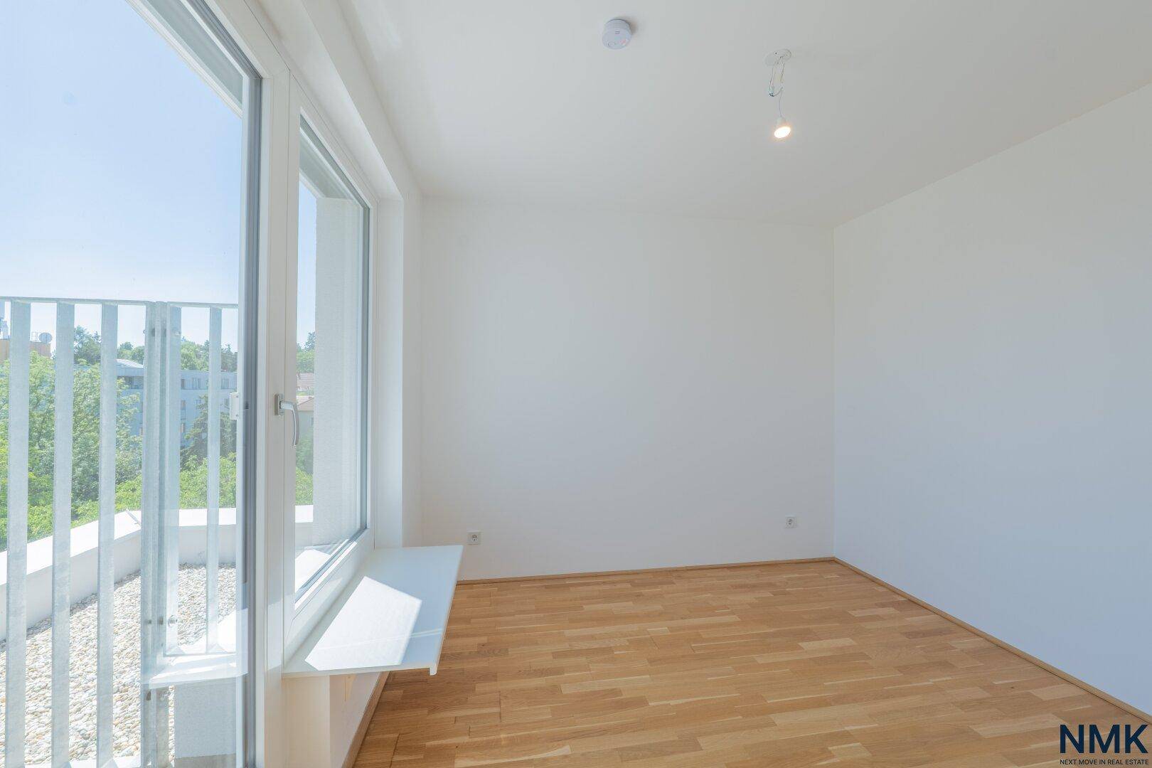 Lichtdurchfluteter Raum mit hellem Parkettboden und breiter Fensterfront zum Außenbereich.