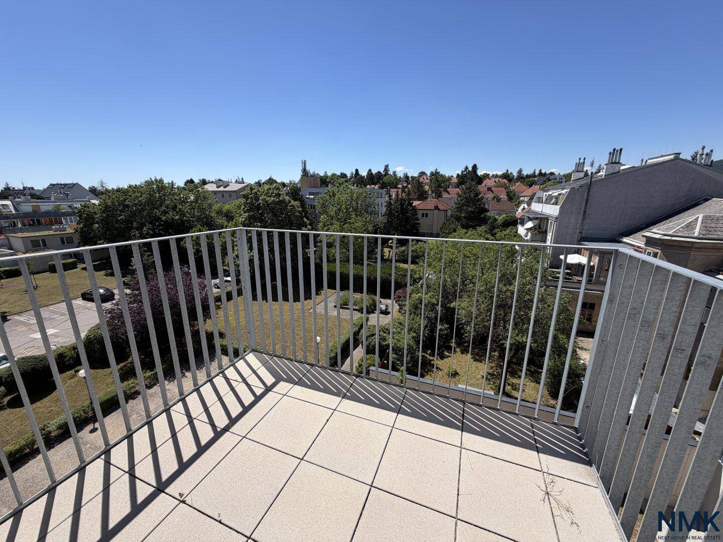 Heller Balkon mit Metallgeländer und Ausblick auf die grüne Umgebung und weitere Gebäude.